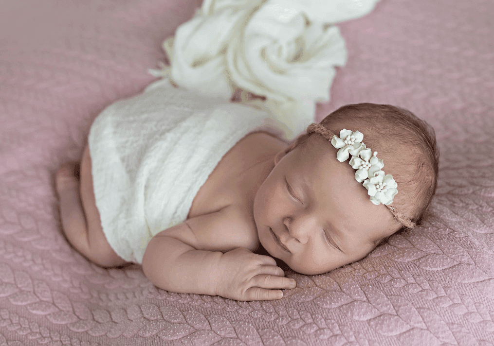 Vnučka Valinka jako newborn — spící miminko v bílém s květinovou čelenkou